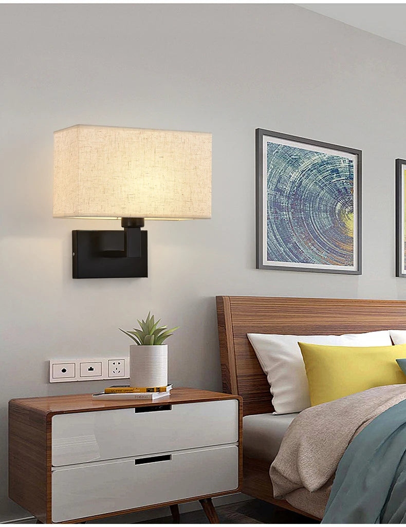 Modern bedroom with wooden nightstand, wall lamp, and bed with colorful pillows.