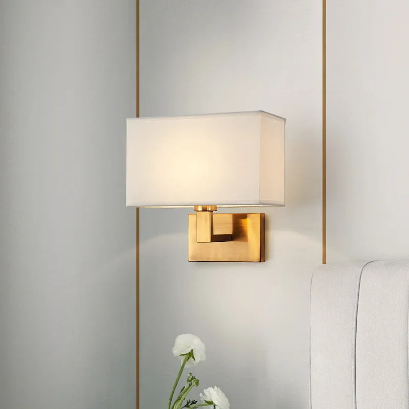 Gold wall sconce with a white lampshade on a neutral wall.