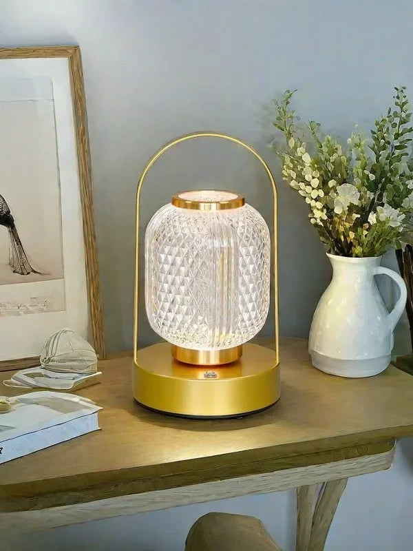 Decorative table lamp with gold base and clear glass shade on a wooden surface.