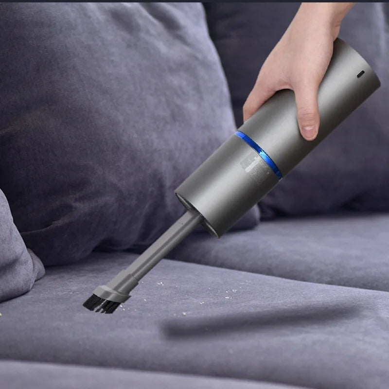 Hand holding a handheld vacuum cleaner on a gray couch