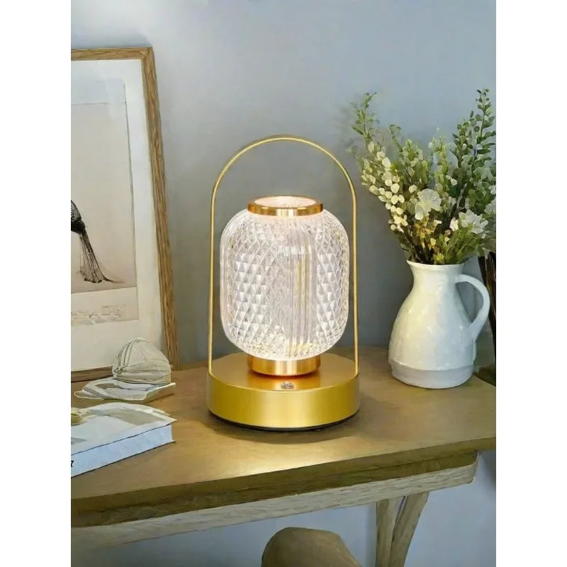 Decorative table lamp with gold base and clear glass shade on a wooden surface.