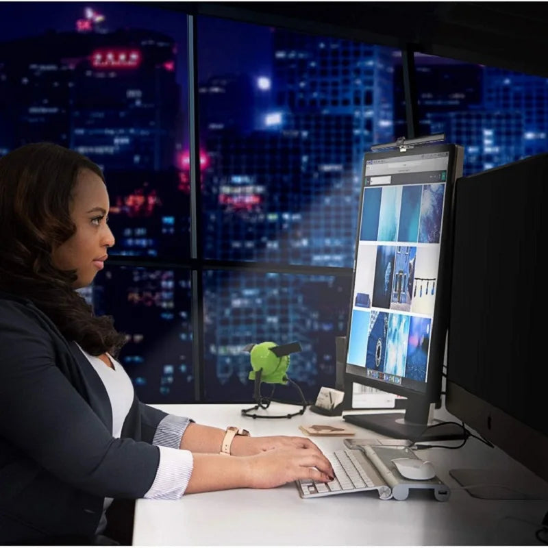 Woman working at a desk with multiple computer monitors in an office setting.